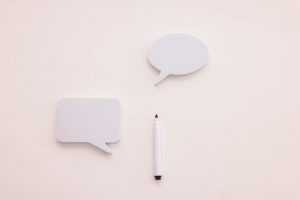 Minimalist image of two blank speech bubbles and a marker on a clean, white background.